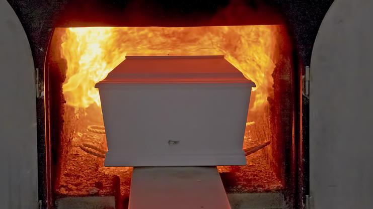 Einäscherungsanlage mit einem weißen Sarg, der in einen brennenden Ofen geschoben wird.